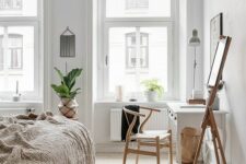 a Nordic bedroom with a bed with neutral bedding, a white vintage desk, some potted plants and chic vintage decor