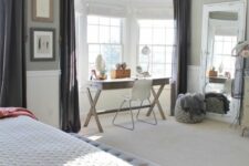 a beautiful grey bedroom with a large bed, a grey bench, a bay window and a trestle desk there, a white chair, a driftwood lamp