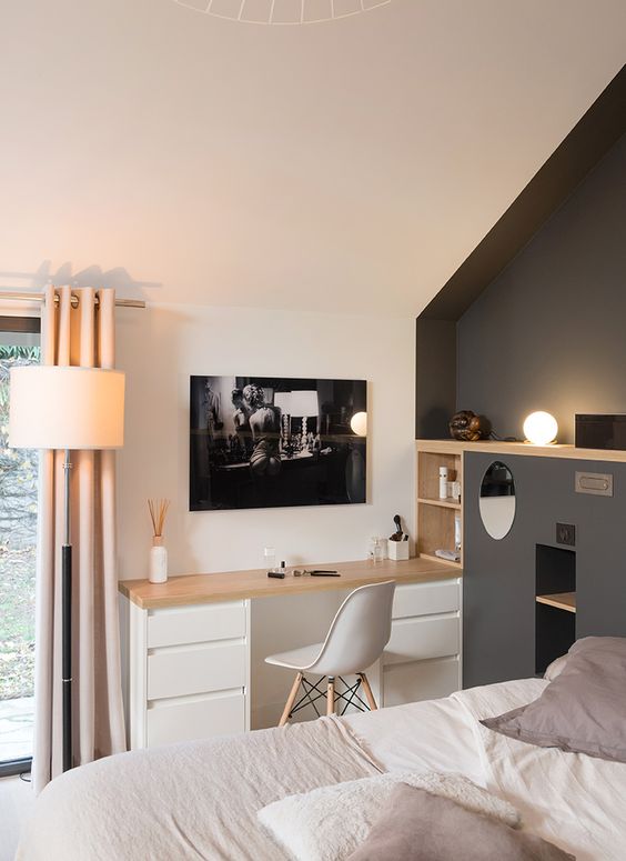 A bedroom with a grey accent wall, a small built in desk, built in shelves, a bed with neutral bedding and some decor