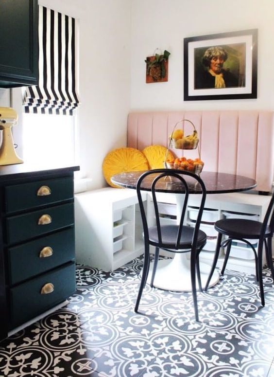 a bright breakfast nook with a corner seat with a pink back, a black table and chairs and a gallery wall