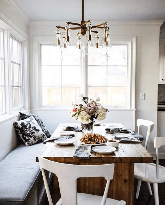 a chic breakfast nook or dining space with a corner sofa and a wooden table is filled with natural light