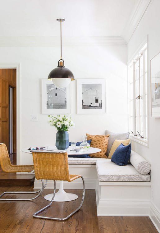 a chic modern breakfast corner with a corner seat and pillows, a round table, woven chairs, a vintage pendant lamp and some artwork