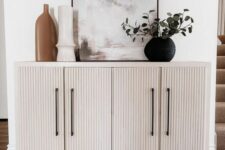 a chic white credenza of an IKEA Kallax piece with elegant fluted doors, black legs and black handles is very stylish