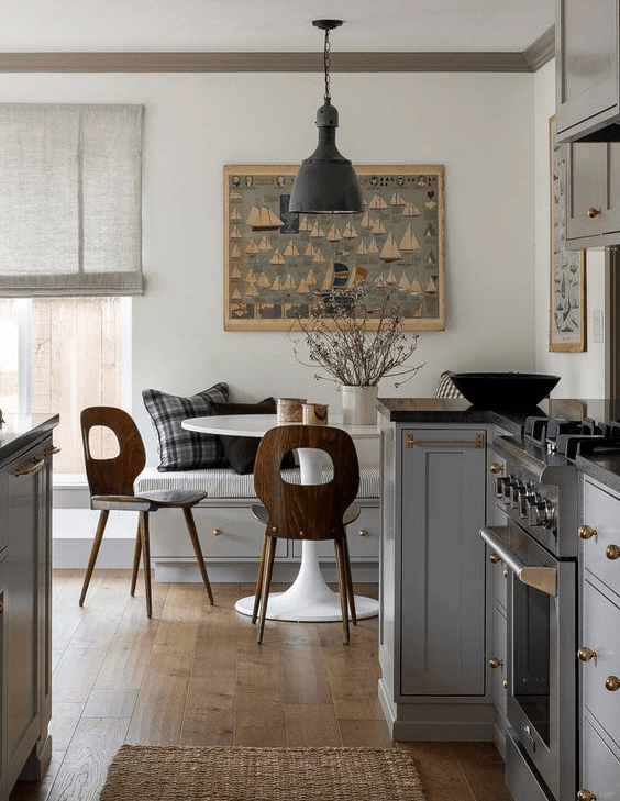 a cool modern farmhouse kitchen with grey cabinets, black countertops, a dining zone in the corner with a bench and a white table plus chairs