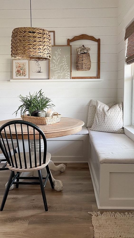 a cottage breakfast corner with  a corner seating and pillows, a stained round table, a woven pendant lamp and a ledge gallery wall