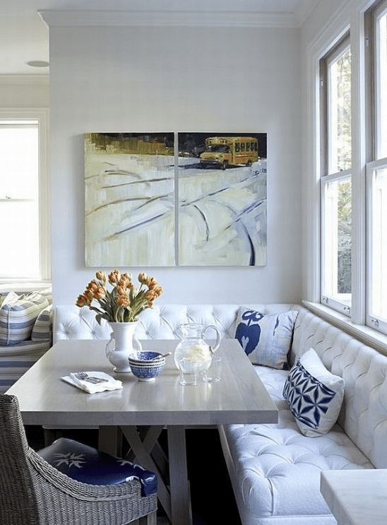 a cozy breakfast nook with a white corner seating, a neutral table and woven chairs, a mini gallery wall and some blooms