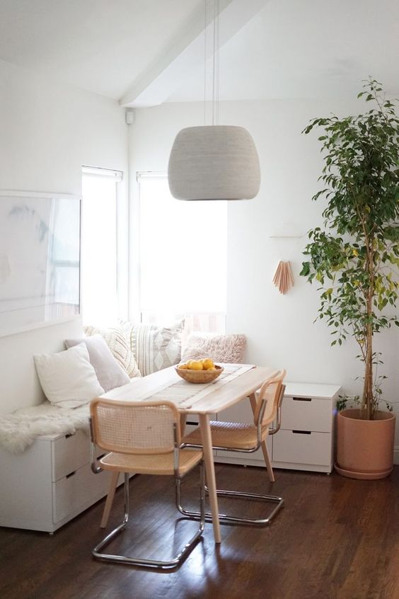 a cozy modern breakfast nook with a white storage corner bench, a table and cane chairs, a pendant lamp and some art