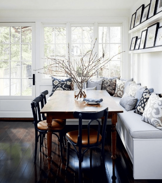 a farmhouse breakfast nook with a corner banquette seating, a stained table and black chairs, a ledge gallery wall