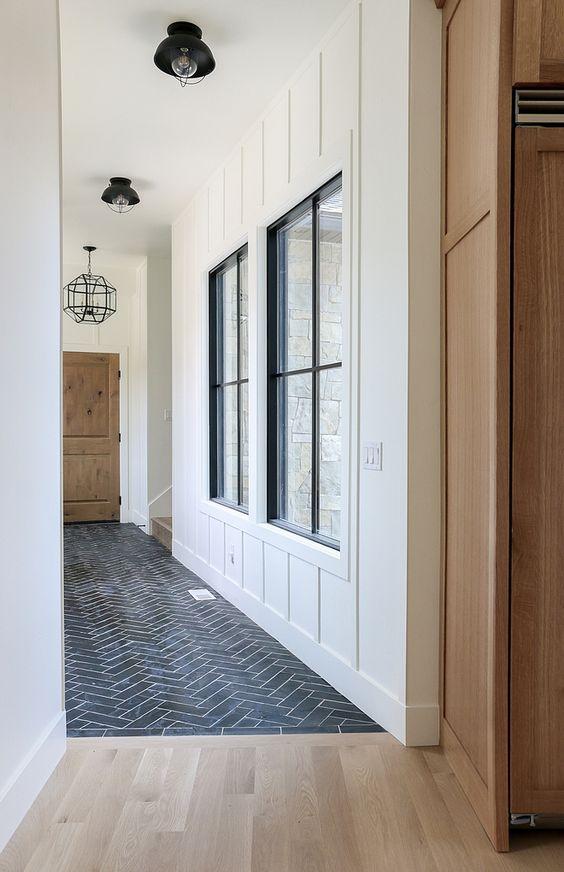 A hallway clad with black herringbone tiles transitioning into light stained laminate without any borders for a modern feel