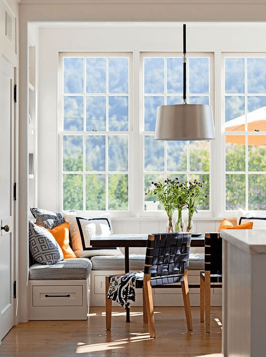 a light-filled breakfast nook with a corner banquette seating, a dark table, woven chairs and a pendant lamp is lovely
