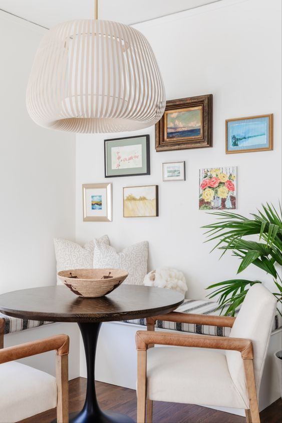 a lively breakfast corner with a corner seating, a stained table and creamy chairs, a pendant lamp and a bright gallery wall