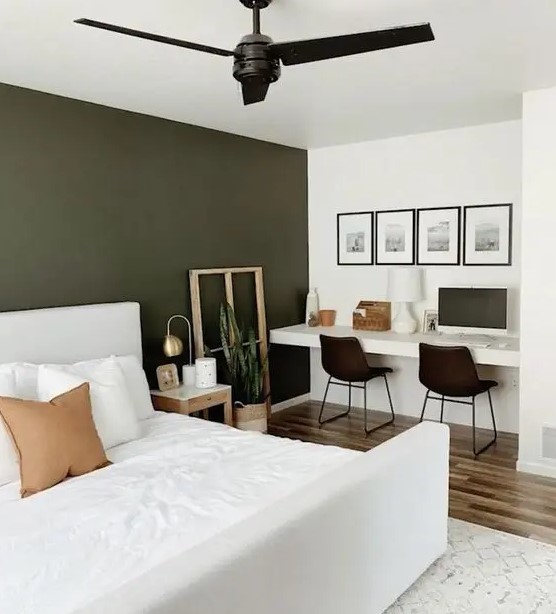 A lovely and functional bedroom with an olive green accent wall, a white bed with bedding, built in desk, black chairs and a gallery wall