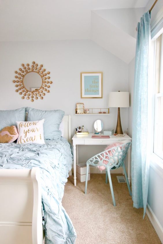a lovely bedroom with a small desk and a blue chair, a neutral bed with blue bedding, some cool decor and brass touches