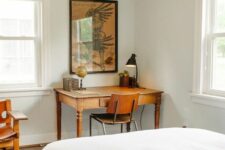 a mid-century modern bedroom with a bed with neutral bedding, a small vintage desk and stained chairs, a printed rug and artwork