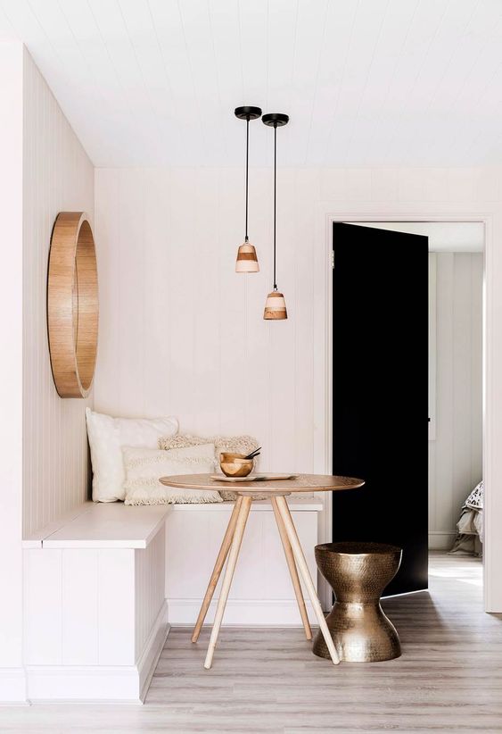 a minimal breakfast corner with a white corner seating, a stained table, a brass metal stool, pendant lamps and a mirror in a wooden frame