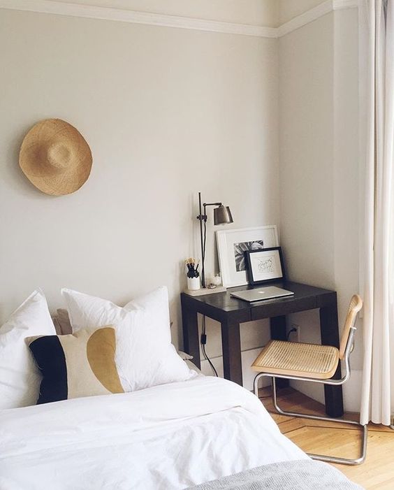 a modern bedroom with a bed and neutral bedding, a black desk and a cane chair, some boho decor