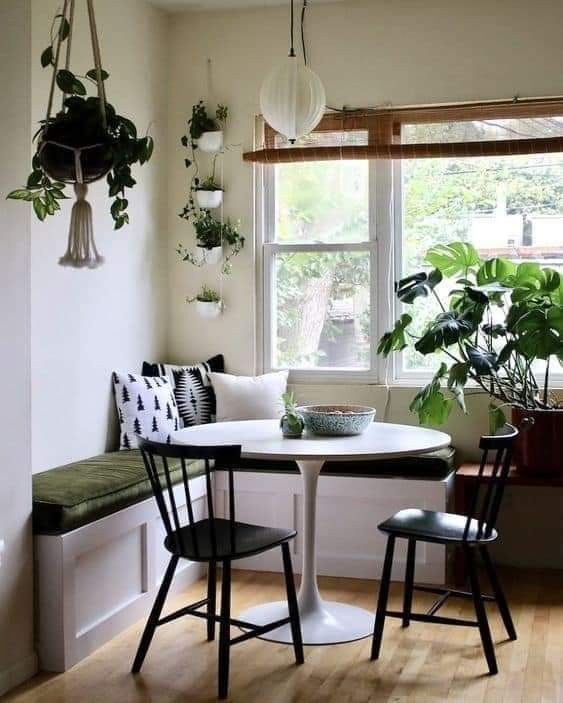 a modern boho breakfast nook with a corner seating, a white table, black chairs, potted plants and some light