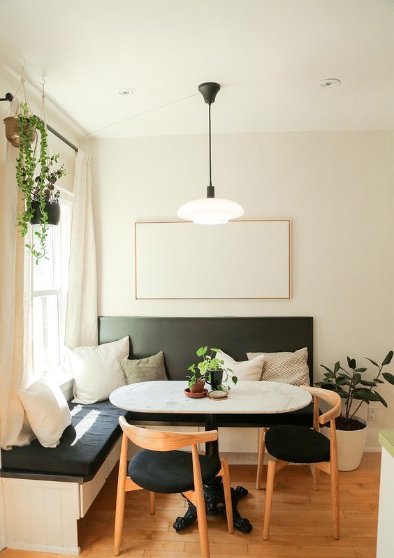 a modern breakfast nook with a black corner seating, an oval table, black chairs, potted plants and a pendant lamp