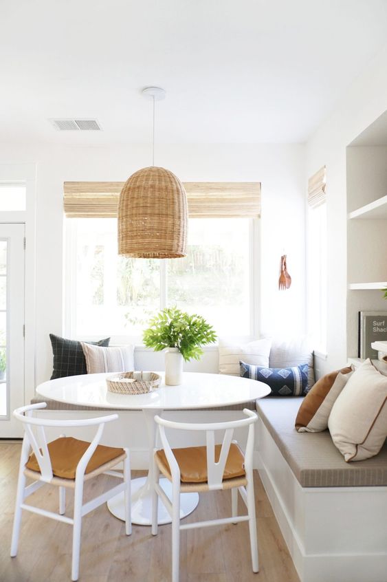 a modern farmhouse breakfast nook with a corner seating, a round table and white chairs, a woven pendant lamp