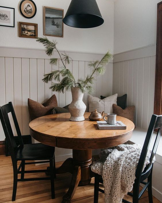 a modern farmhouse breakfast nook with a corner seating, a stained round table, black chairs, a black lamp and a gallery wall