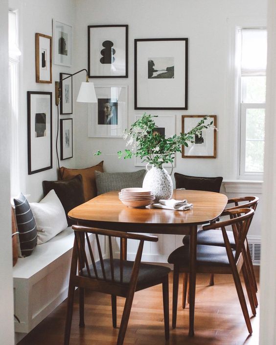 a modern farmhouse breakfast nook with a corner seating with pillows, a stained table and chairs and a cool corner gallery wall