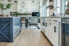 a modern farmhouse kitchen with white cabinetry and a blue kitchen island, floor transition from laminate to hex tiles and cool pendant lamps