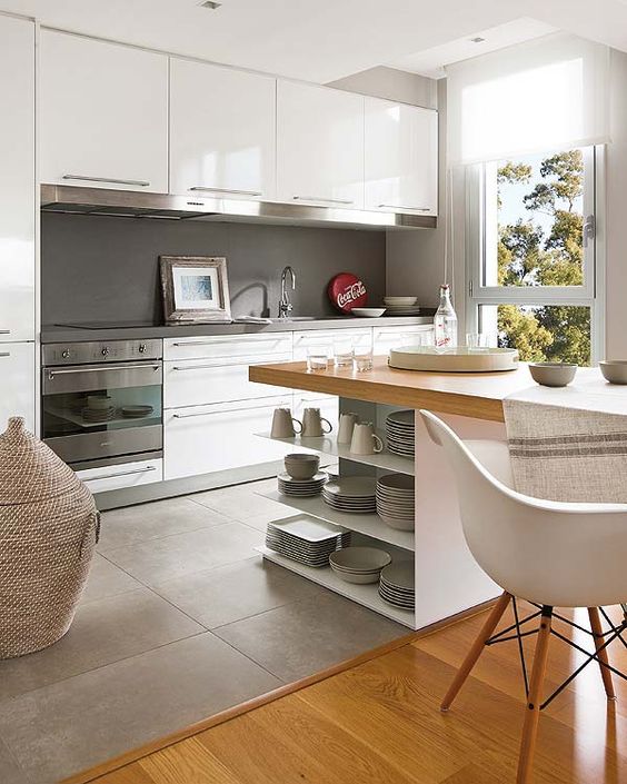 a modern white kitchen with a concrete backsplash, a grey tile floor transitioning into laminate, a kitchen island and chairs