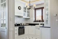 a modern white kitchen with black countertops, a white subway tile backsplash, a black and white tile floor and a laminate floor in the next zone