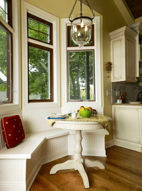 A neutral farmhouse breakfast nook with a built in banquette seating, a small table, some pillows and a pendant lamp