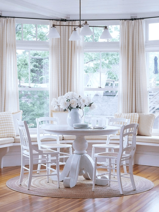 a neutral farmhouse breakfast nook with a white banquette seating, a white table, white chairs and a chandelier