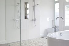 a neutral minimalist bathroom with pebble to tile floor, a shower space, an oval tub and a chandelier