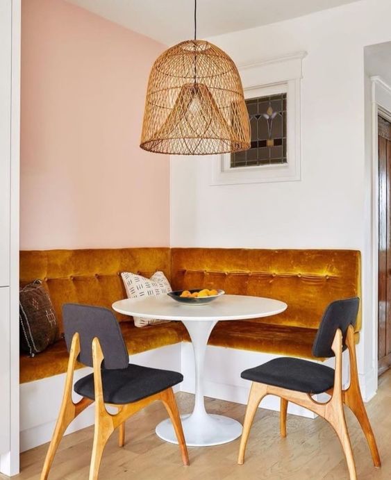 a refined modern breakfast nook with a marigold upholstered bench, a round table, black chairs and a woven pendant lamp