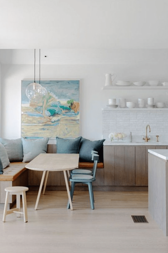 a serene coastal kitchen with whitewashed cabinets, open shelves and a cozy dining zone with blue pillows in the corner