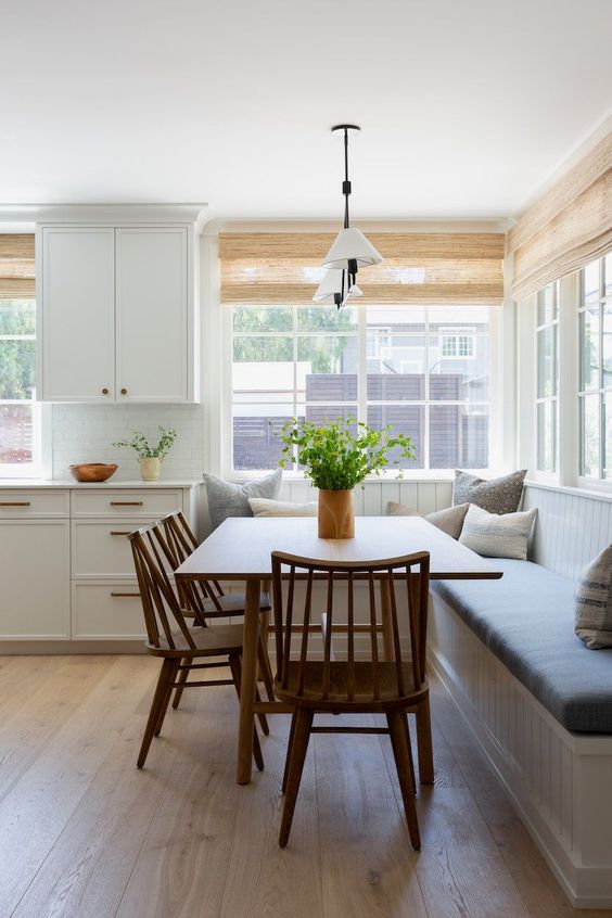 a serene modern farmhouse breakfats nook with a corner seating, a stained table and chairs, a pendant lamp and some pillows