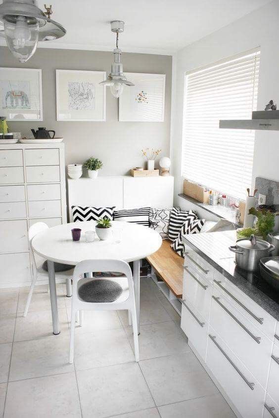 a small Scandinavian breakfast corner with a corner bench and pillows, a white table and chairs and chic decor