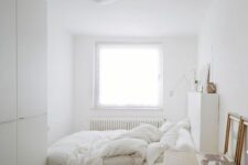 a small and airy white bedroom with a low bed and neutral bedding, a wardrobe, a stained desk and some simple decor