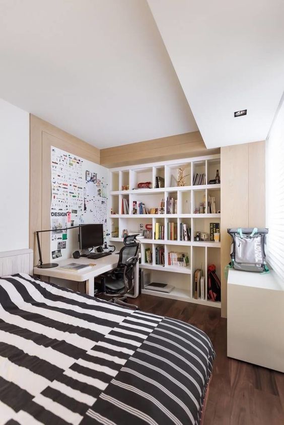 A small yet functional bedroom with built in shelves and a desk, a large bed with printed bedding is amazing
