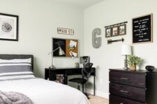 a stylish bedroom with a grey bed and printed bedding, a black desk and a chair, a dark-stained dresser and some decor