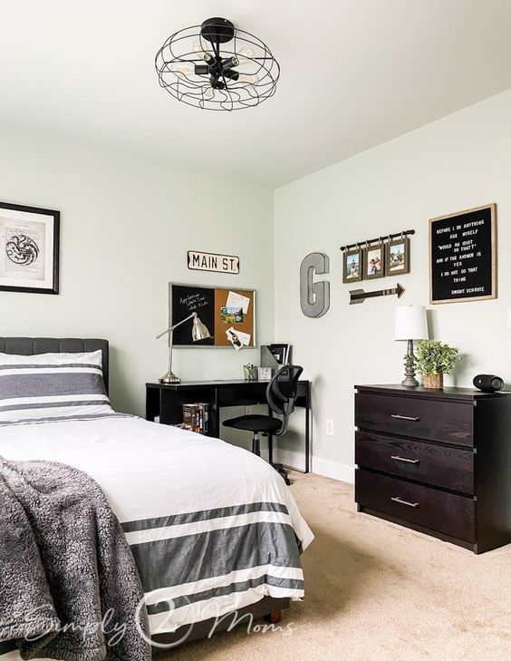 A stylish bedroom with a grey bed and printed bedding, a black desk and a chair, a dark stained dresser and some decor