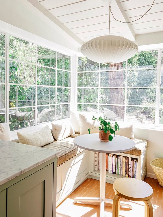 a sunny breakfast nook with a corner seating with storage, a small table and a stool plus a pendant lamp is lovely