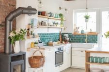 a welcoming kitchen with low white cabinets, a green subway tile backsplash, wooden beams, a kitche island, a floor from tiles to laminate