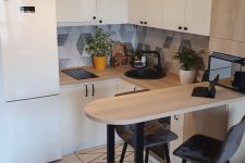 a white Scandinavian kitchen with sleek cabinets, a counter kitchen island, black stools, a tile floor and laminate, with a little border
