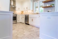 a white modern farmhouse kitchen with a grey subway tile backsplash, a hexagon tile floor and a laminate one in the next zone