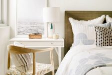 an airy bedroom with a stained bed and neutral bedding, a tiny white desk and a nightstand, some decor and artwork