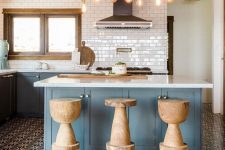 an eye-catchy kitchen with blue cabinetry, a kitchen island, cork stools, a floor transition with black and white tiles and laminate