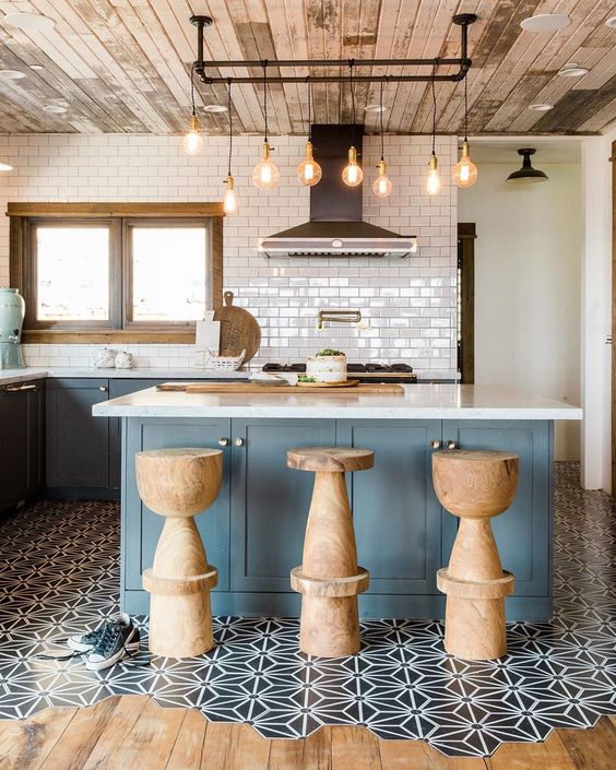 An eye catchy kitchen with blue cabinetry, a kitchen island, cork stools, a floor transition with black and white tiles and laminate