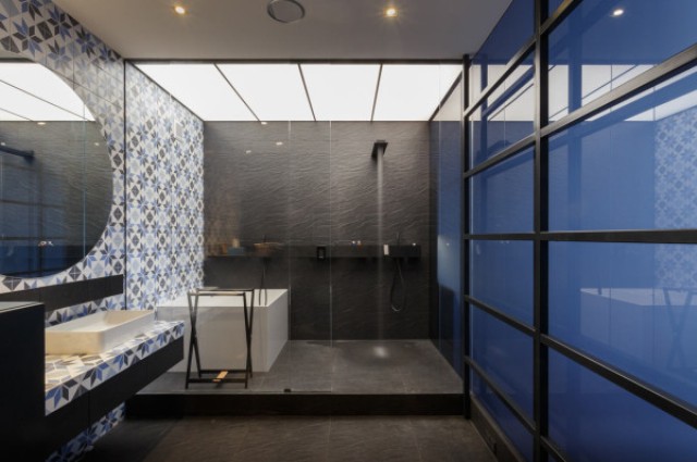 The shower fixtures match the color of the dark tiles behind it, which continue onto the floor of the bathroom