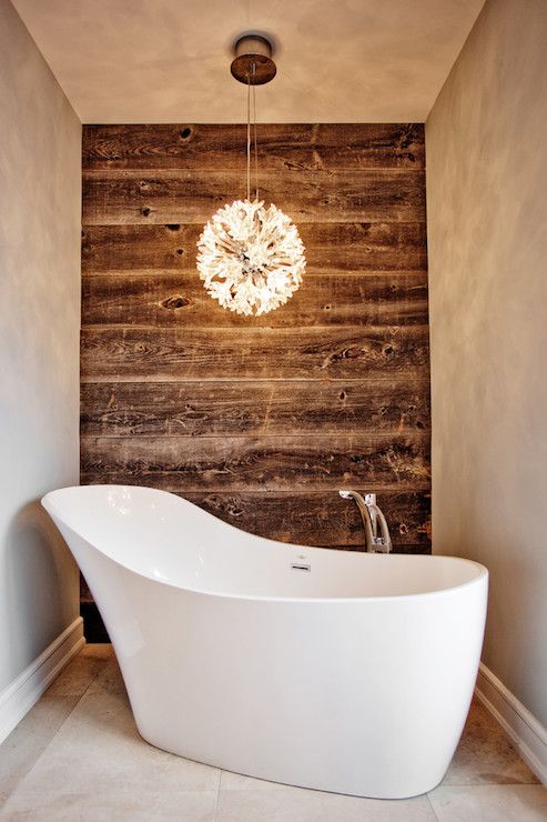worn wood wall contrasts with a modern bathtub and chandelier