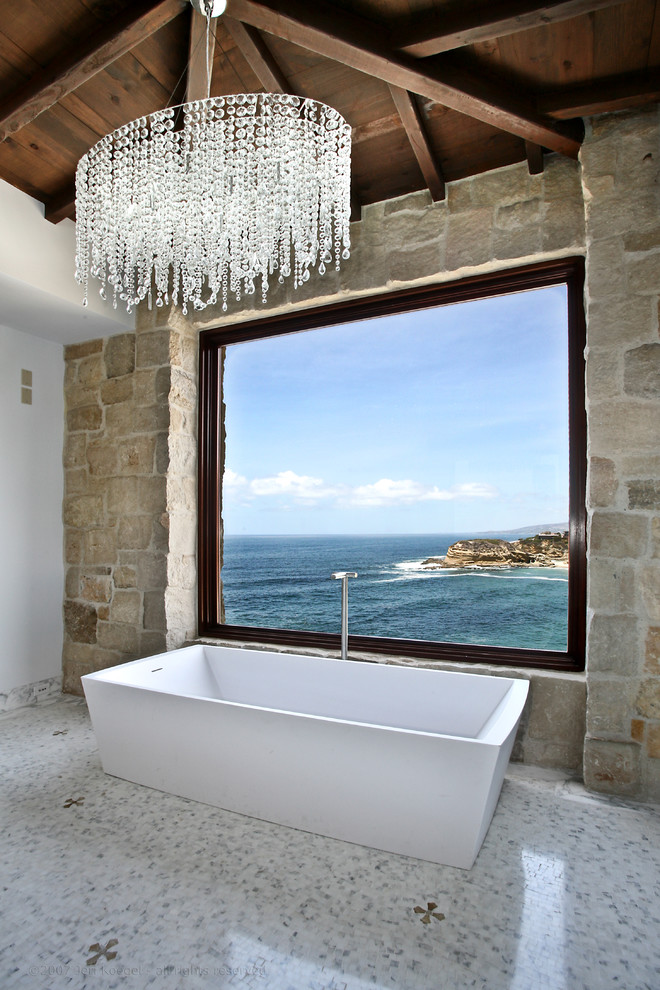 Antique stone wall looks amazing in a contemporary luxurious bathroom. It amazingly frames sea views. (Ancient Surfaces)