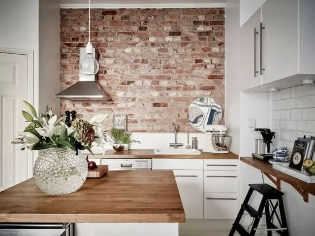 rough brick wall creates a bold accent in this modenr white kitchen and makes it look cool